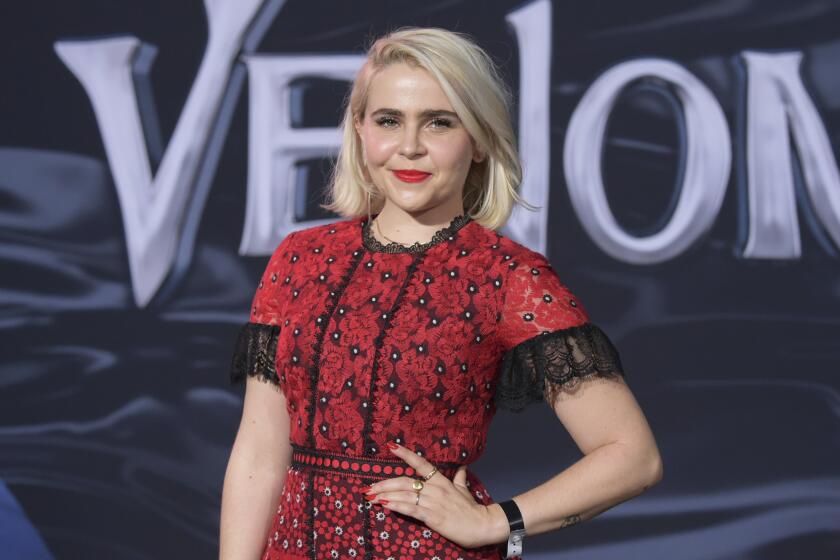 Mae Whitman poses in a red gown with her left hand on her hip