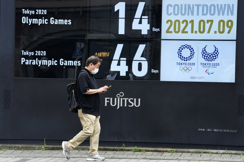 A man wearing a face mask walks past the countdown clock for the Tokyo 2020 Olympic and Paralympic Games near the Shimbashi station, Friday, July 9, 2021, in Tokyo. (AP Photo/Eugene Hoshiko)