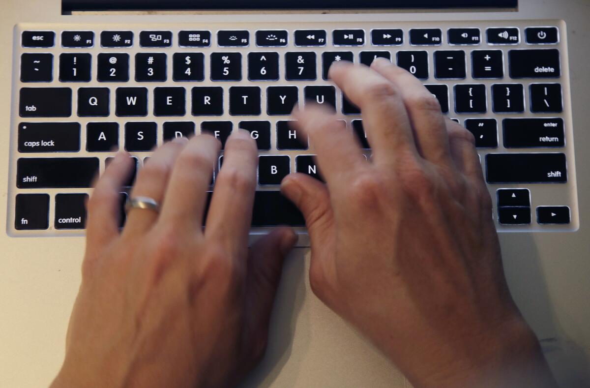 Fingers type on a laptop keyboard.