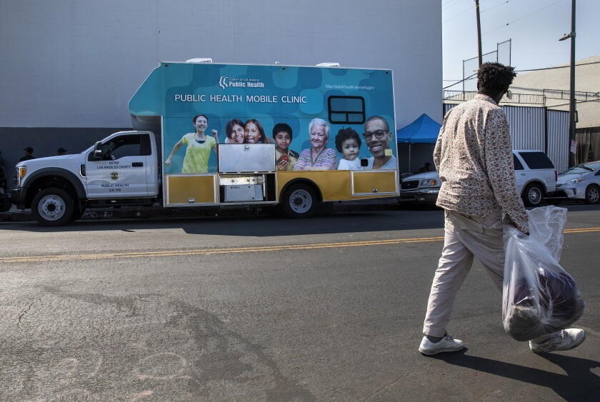 A person carrying a large plastic bag looks at a mobile clinic truck across the street