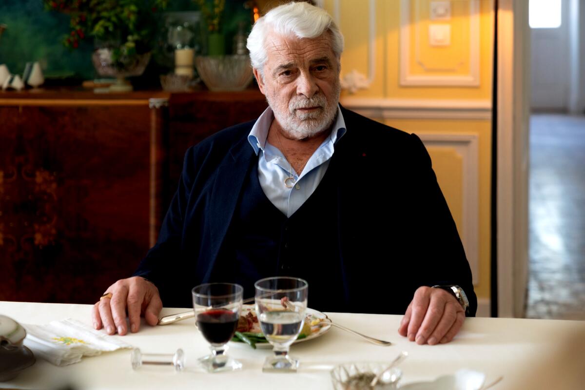 A distinguished elder man sits at a dining-room table.