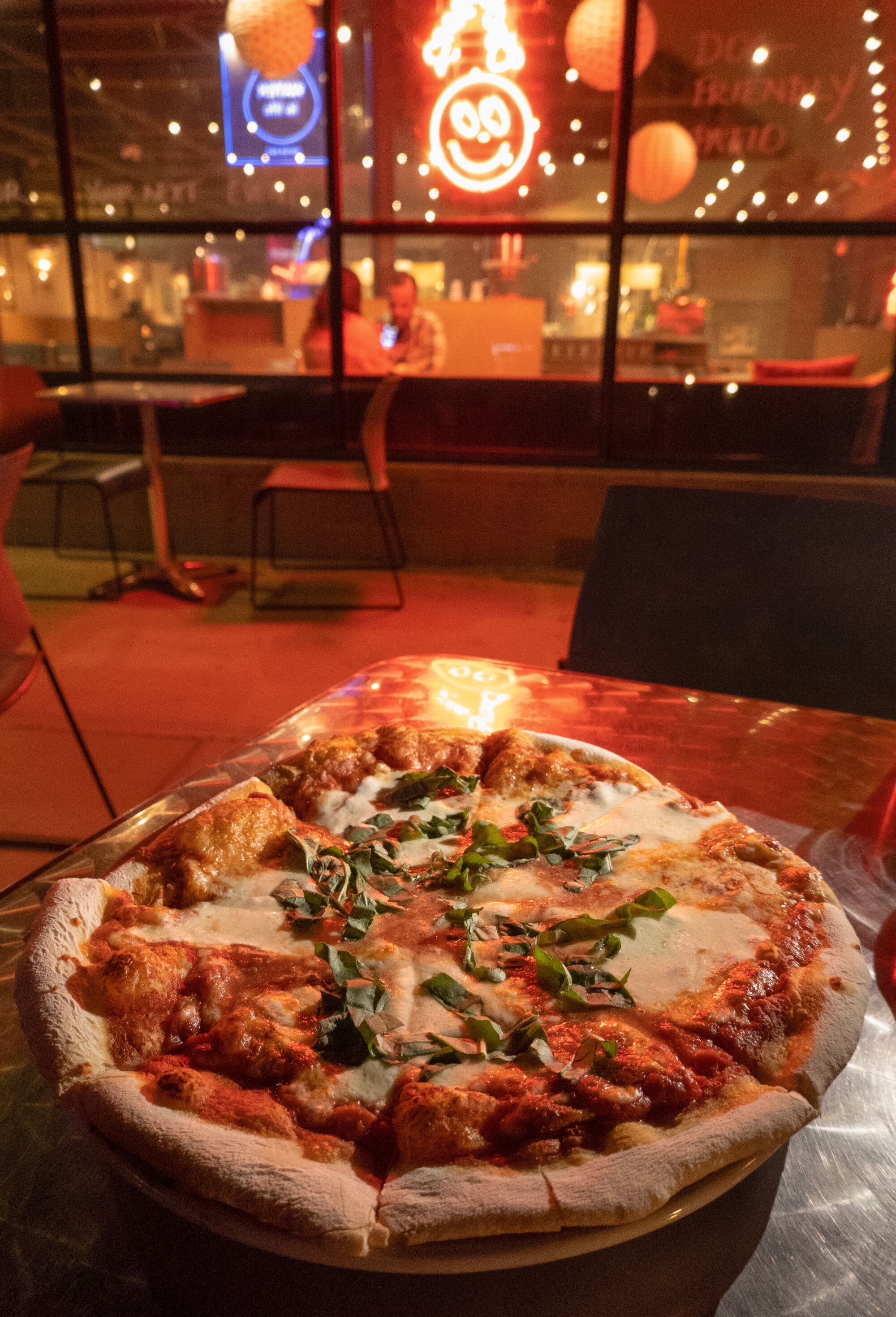 A wood-fired pizza on a table, with red neon lights in the background.