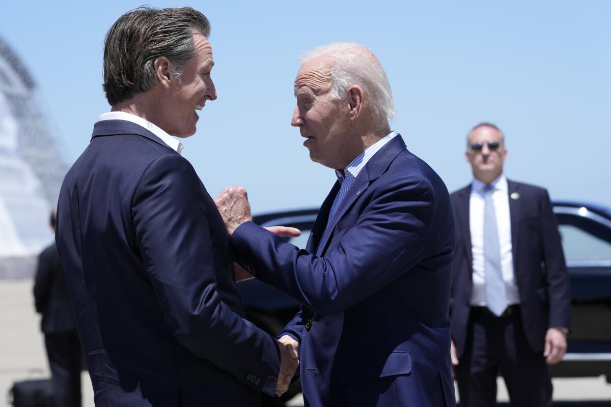 California Gov. Gavin Newsom and President Biden shaking hands outdoors as a man stands by in front of a black car