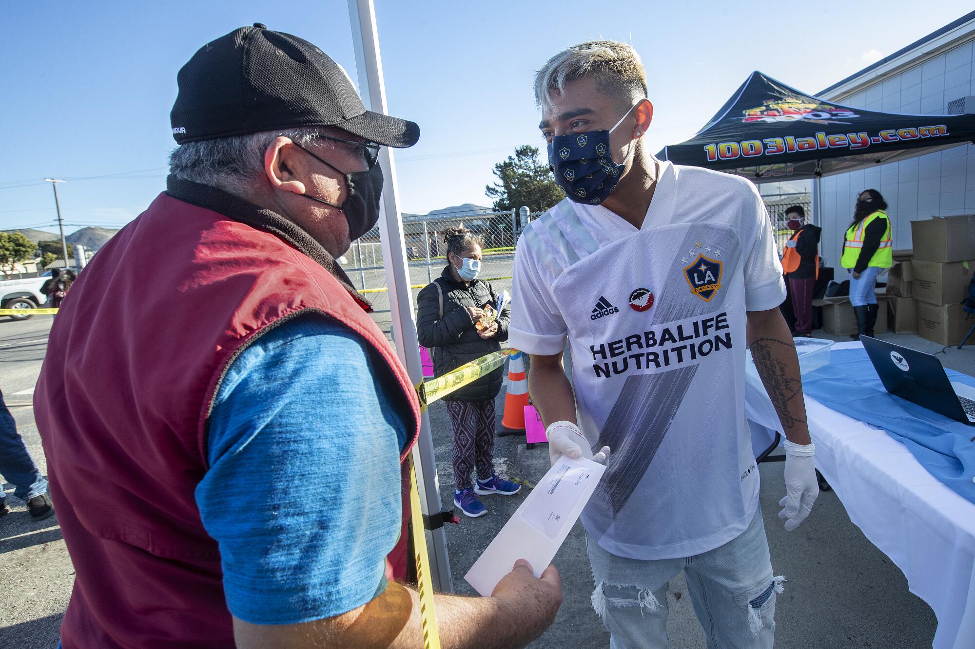 Antonio Tamayo receives an envelope containing a $100 prepaid card from Los Angeles Galaxy soccer player Julian Araujo.