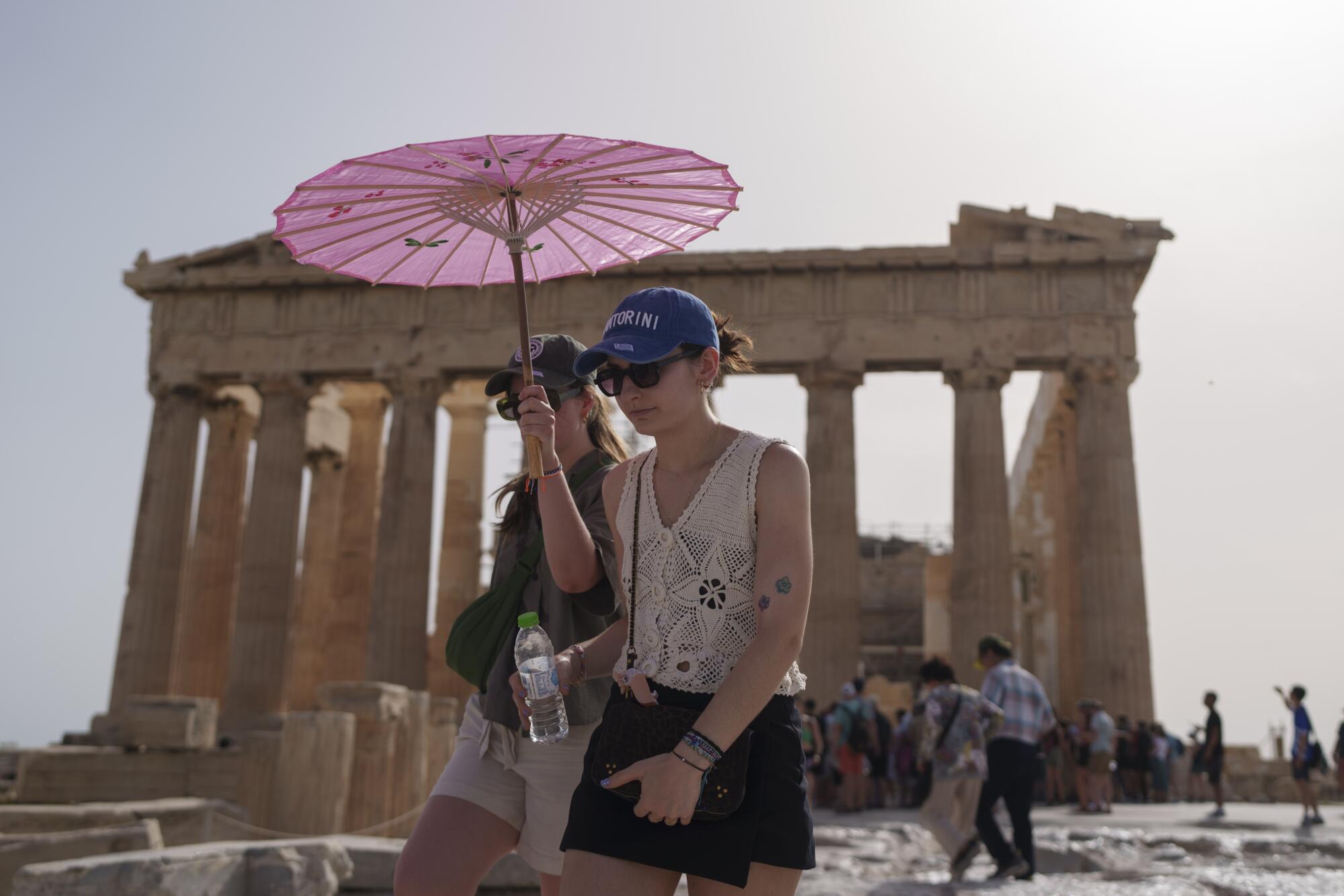 Two women walk beneath a pink parasol as the Parthenon looms in the background.