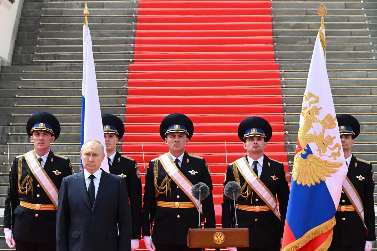 Russian President Vladimir Putin backed by a ceremonial armed guard in from a long stairway covered in a red carpet.