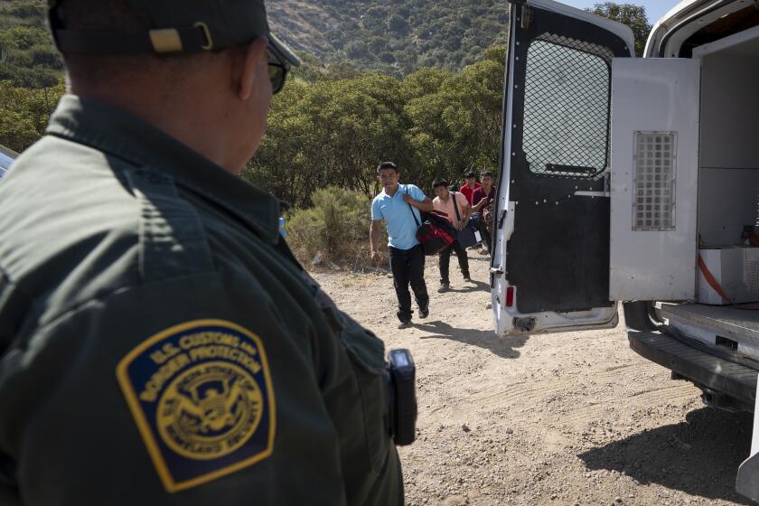 A Border Patrol agent leads a group of migrants seeking asylum towards a van to be transported and processed, Wednesday, June 5, 2024, near Dulzura, Calif. President Joe Biden on Tuesday unveiled plans to enact immediate significant restrictions on migrants seeking asylum at the U.S.-Mexico border as the White House tries to neutralize immigration as a political liability ahead of the November elections. (AP Photo/Gregory Bull)
