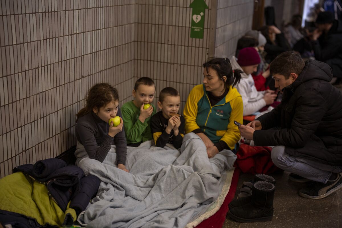 A family sheltering in a Kyiv subway station sits on the floor eating fruit