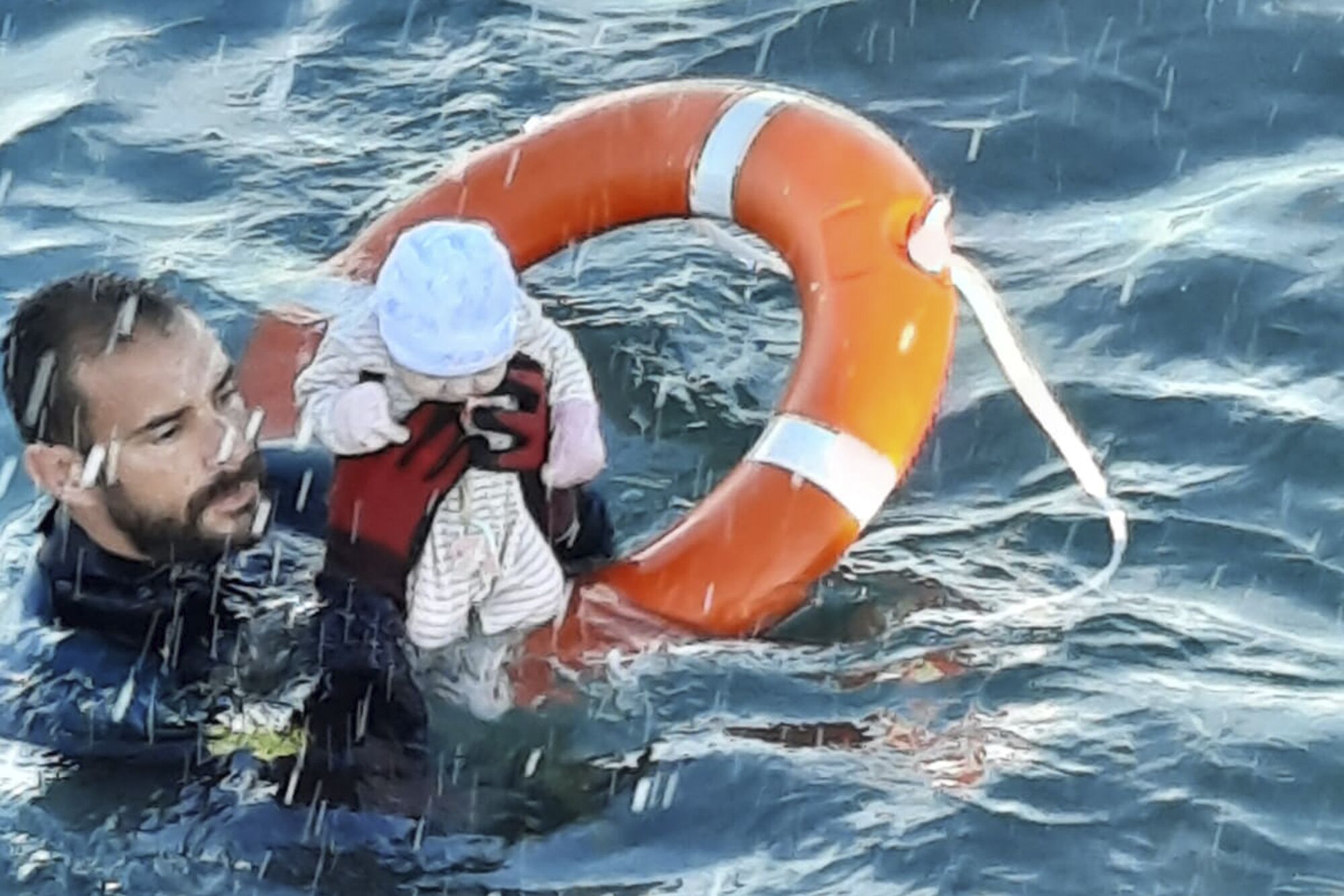 A man holds up a baby in both hands while floating in the sea on an orange life preserver ring