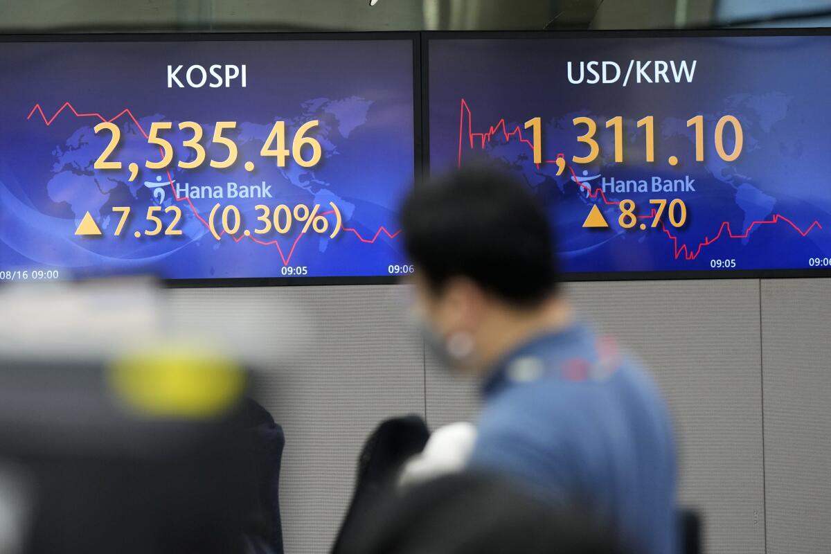 A currency trader walks by screens showing the Korea Composite Stock Price Index (KOSPI), left, and the foreign exchange rate between U.S. dollar and South Korean won at a foreign exchange dealing room in Seoul, South Korea, Tuesday, Aug. 16, 2022. Asian shares mostly rose Tuesday after a rebound on Wall Street, despite regional investor risks reflected in negative economic data out of China. The benchmark in Tokyo was little changed, erasing earlier gains, but indexes in South Korea, Australia and China gained in morning trading. (AP Photo/Lee Jin-man)