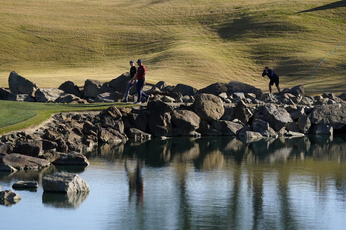 Pro golfers walk past a water feature 