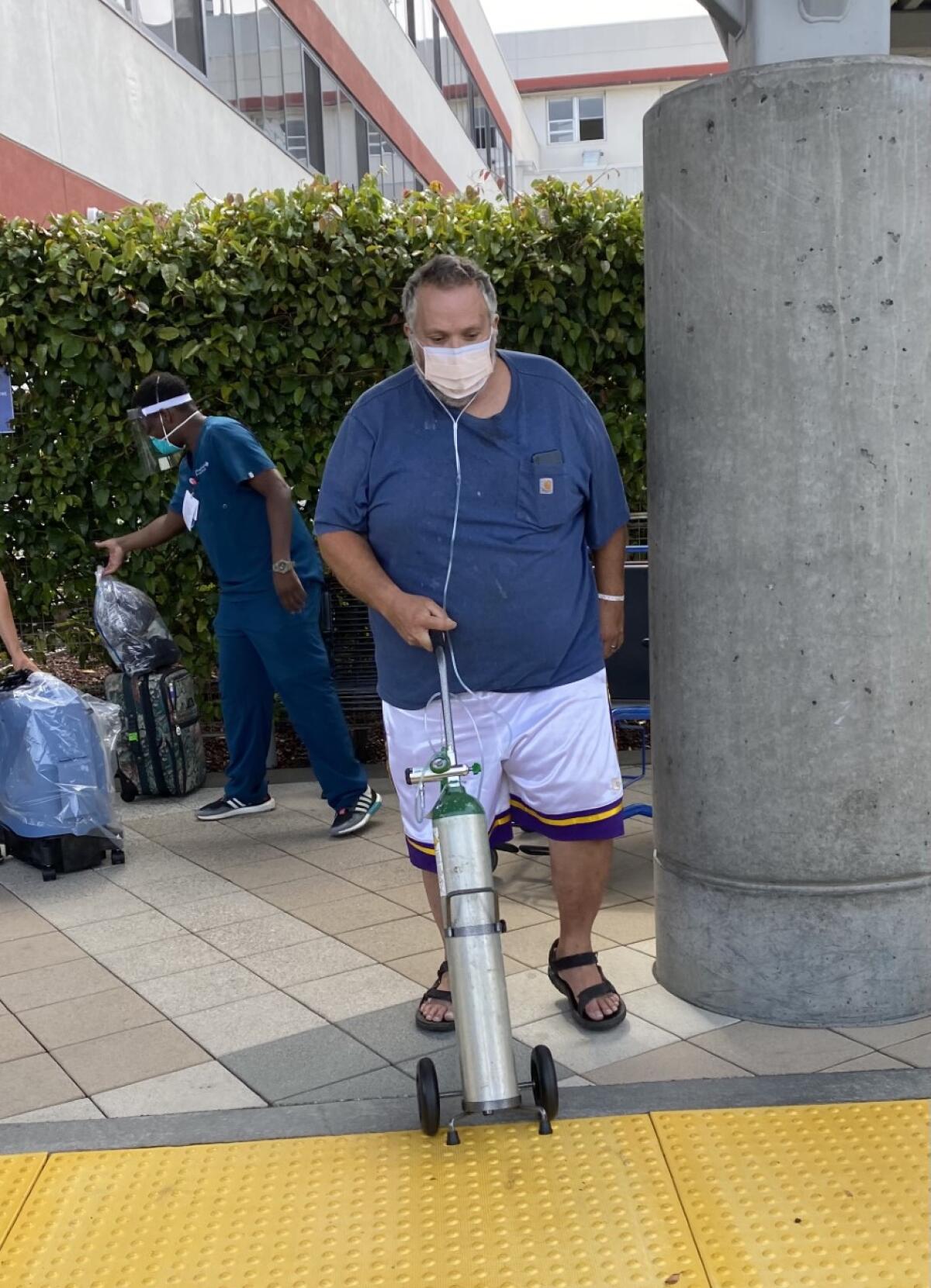 A man walks with a mobile oxygen tank.