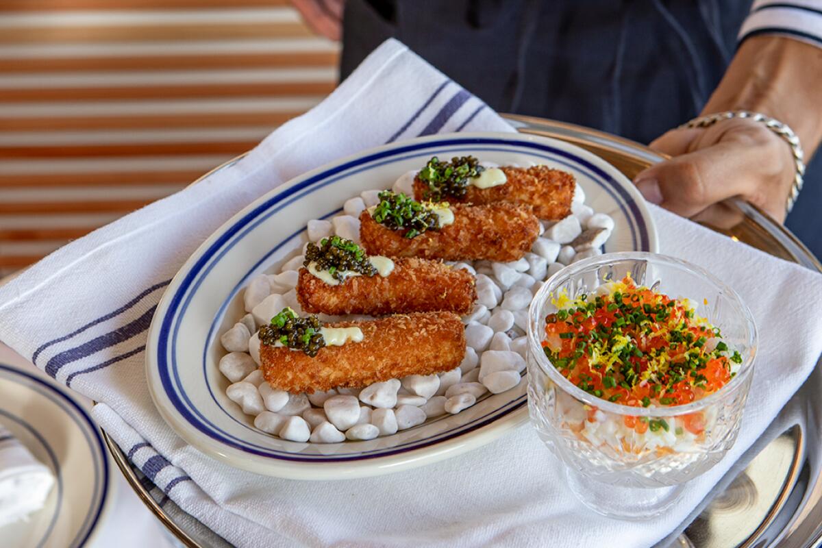 A hand holding out a plate of four caviar-topped fish sticks at Dear Jane's