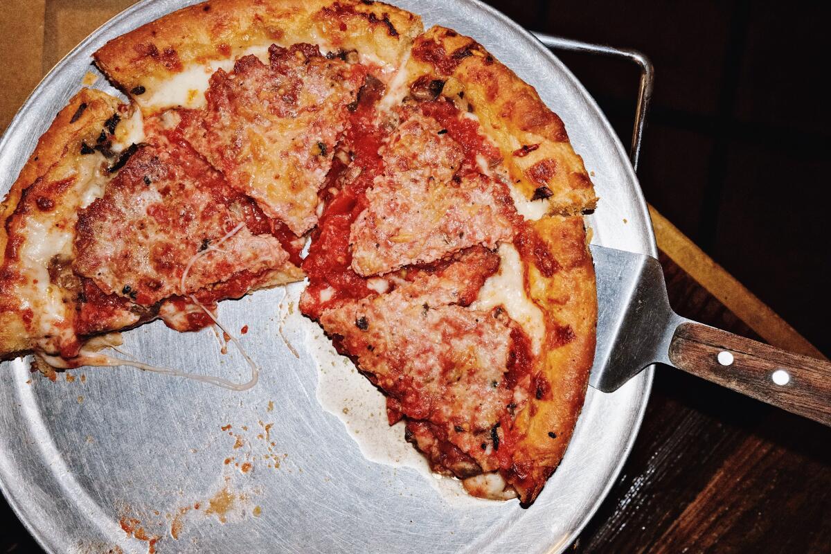 An overhead photo of a Chicago-style deep-dish pizza on a silver tray at Masa of Echo Park. A serving utensil sticks out.