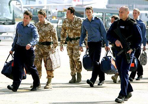 An armed police officer escorts British service personnel, from left, Paul Barton, Joe Tindell, Adam Sperry, Nathan Summers and Simon Massey, as they leave their aircraft at London's Heathrow Airport, after their return from Iran following 13 days in captivity.