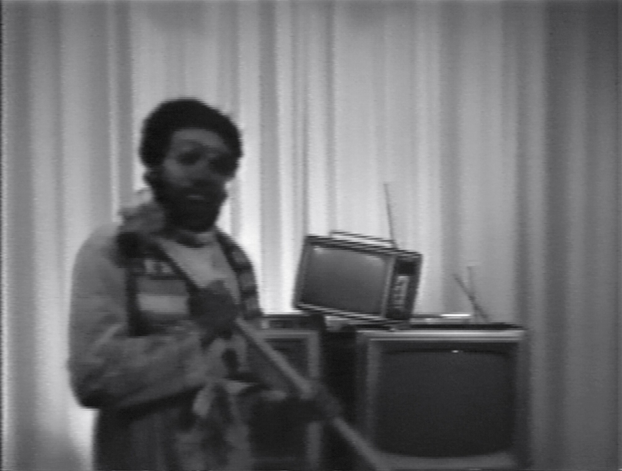 Ulysses Jenkins stands before a stack of TVs wielding a sledgehammer in a grainy black and white video still