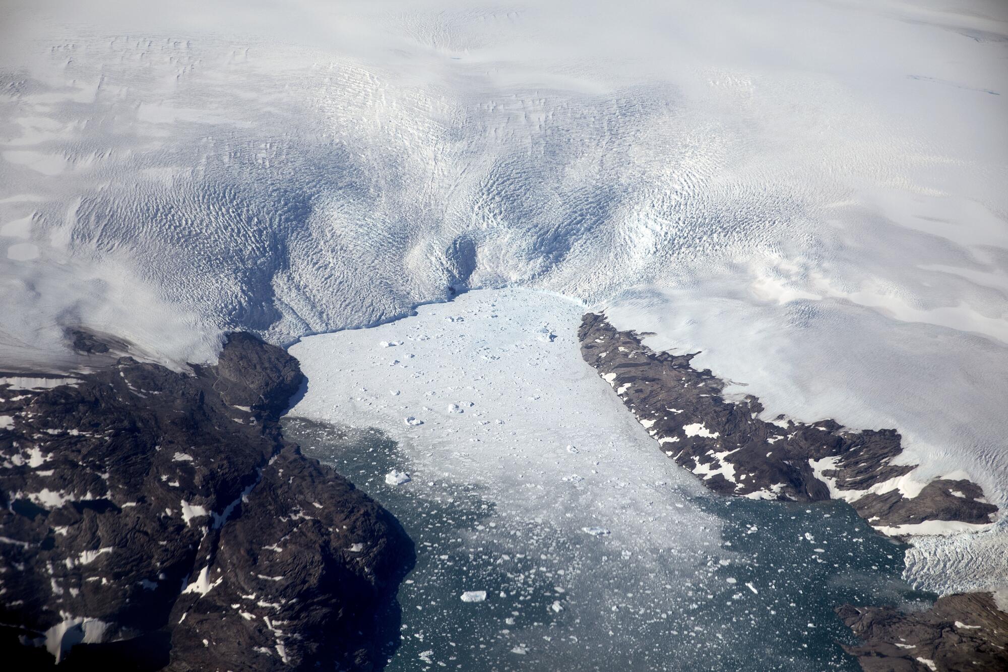 An aerial view of white-covered landscape, with huge chunks of ice breaking off 