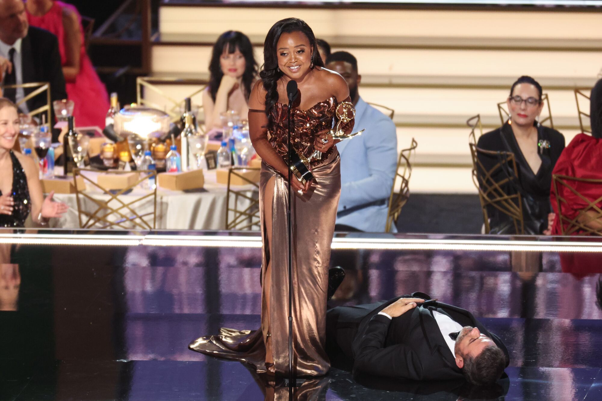 A smiling Quinta Brunson gives an Emmy acceptance speech while host Jimmy Kimmel plays dead on the stage.