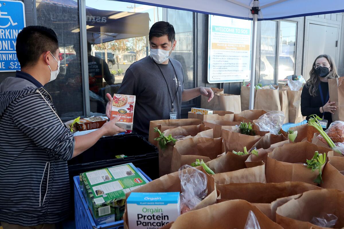 Rudy Ramos, center, SOS chief operations officer, and Don Hoa, left, facilities and safety manager, add items to food bags.