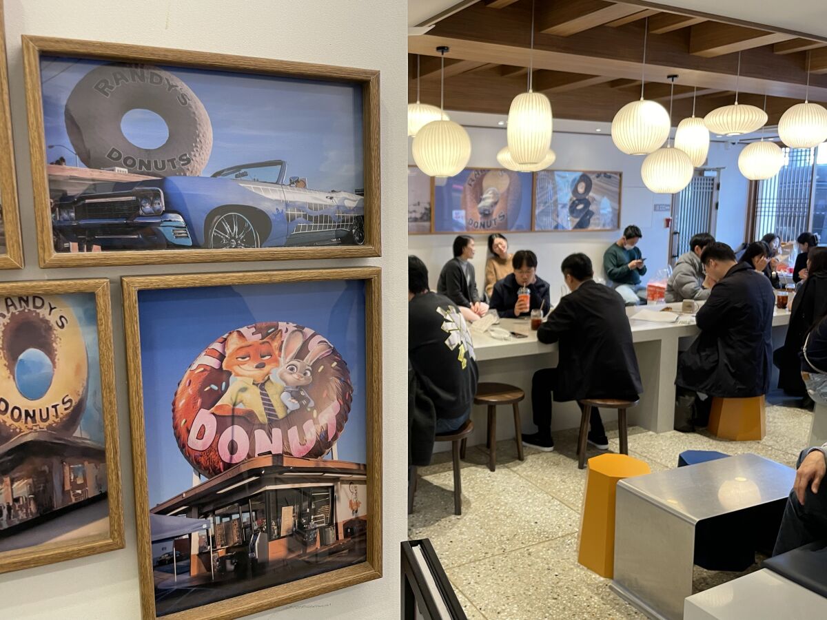 People sit at tables in a shop with framed photos of Randy's Donuts shops.
