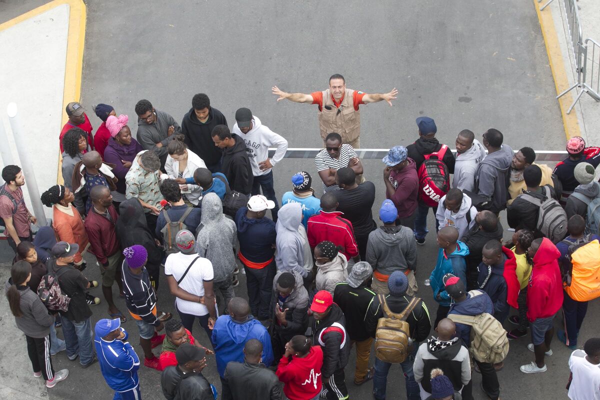 A man in an orange Grupo Beta shirt directs Cameroonian asylum seekers to move away from a gate