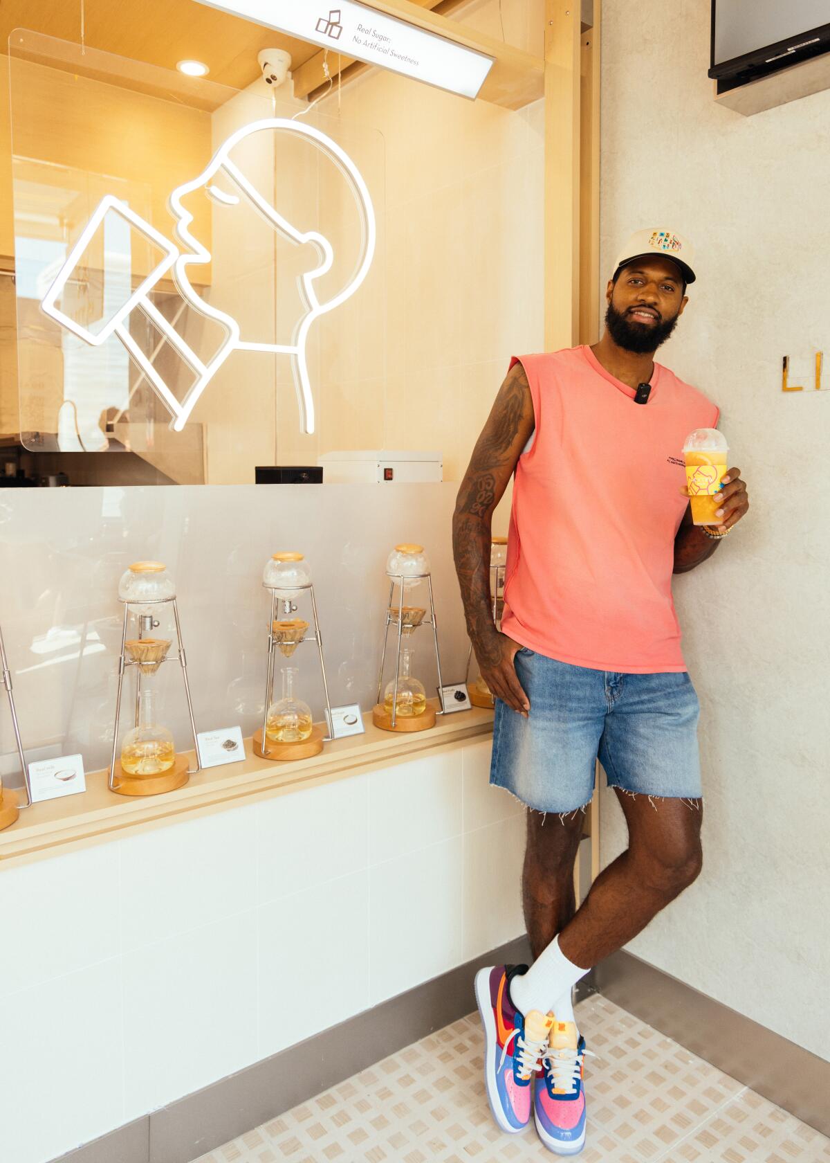 NBA All-Star player Paul George leans against a wall in the tea shop holding a boba tea