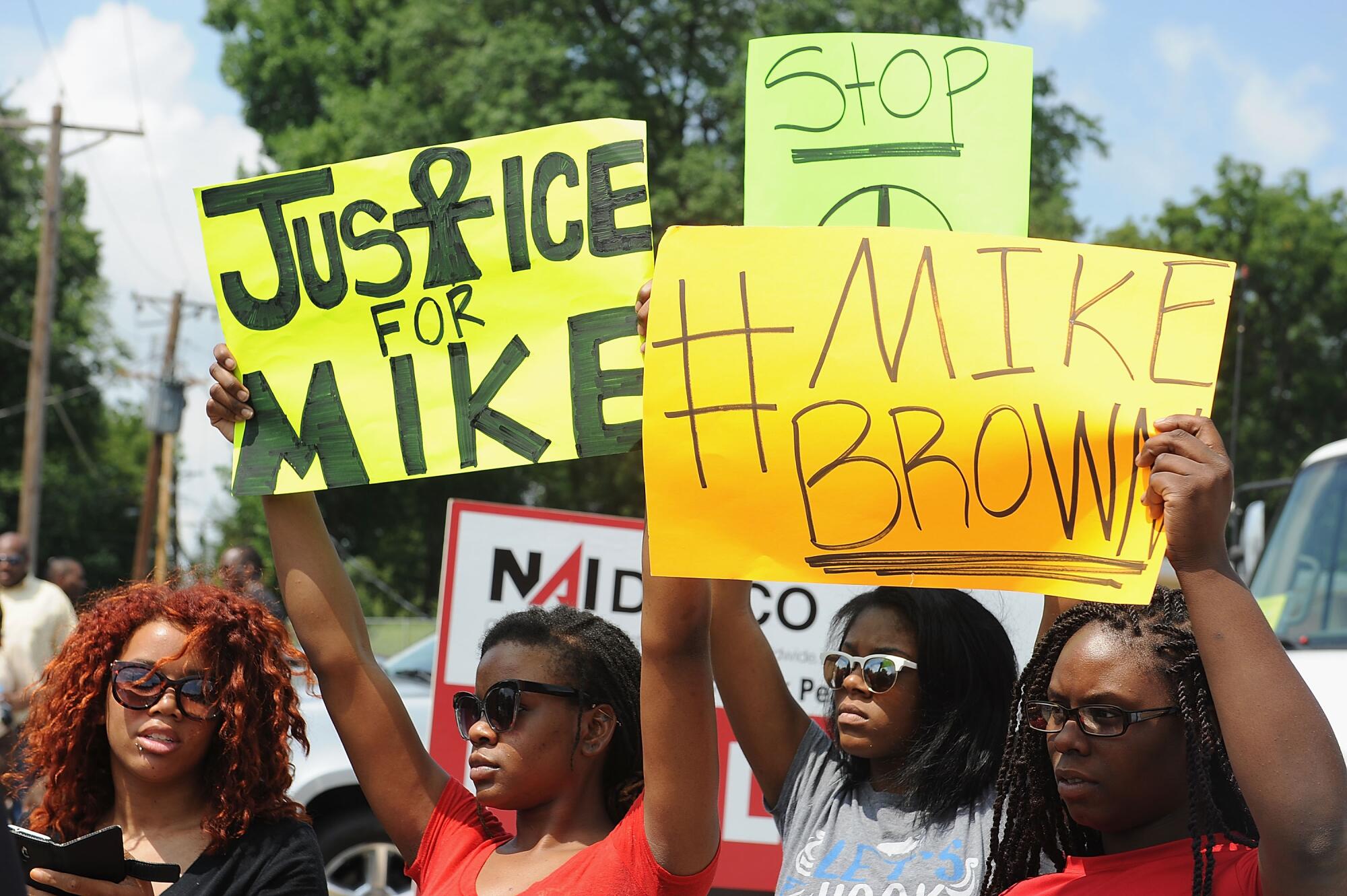 Protesters hold signs, one of which says, "Justice for Mike"