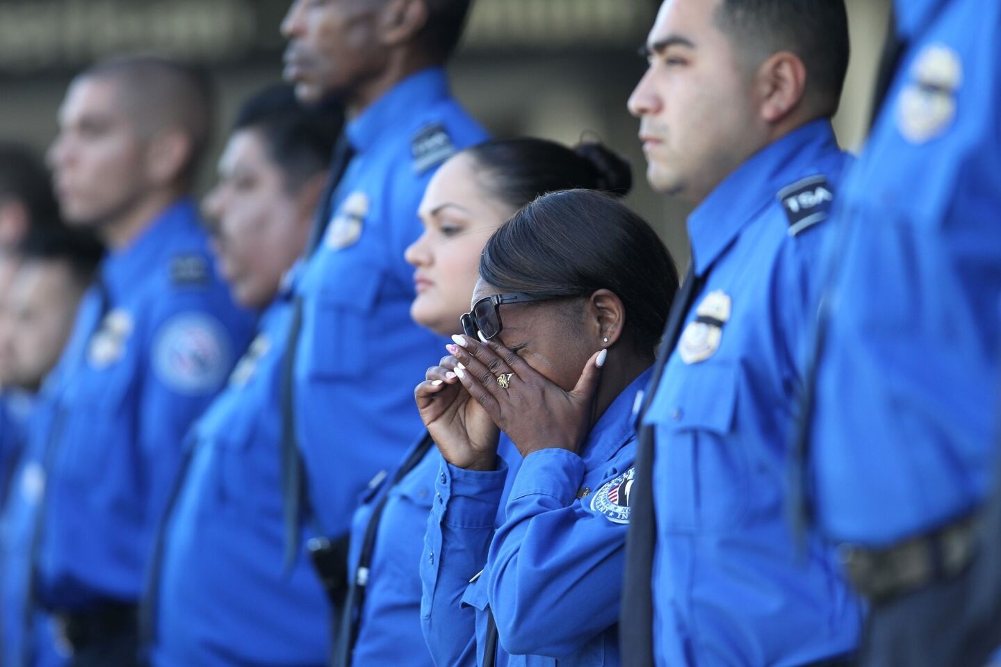 A TSA officer wipes her eyes as an honor guard escorts a U.S. National Honor Flag in a ceremony to memorialize TSA Officer Gerardo Hernandez, who was fatally shot at LAX.