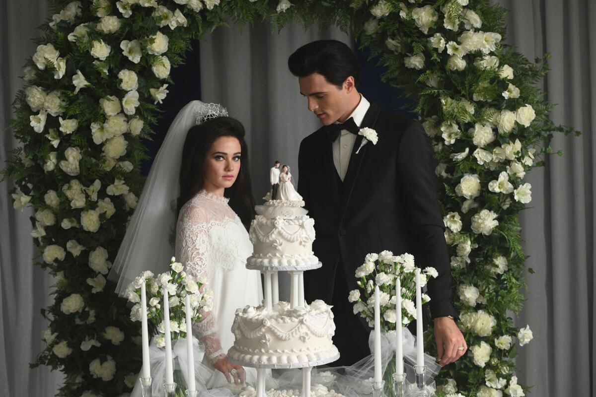 Una novia y un novio detrás de su pastel de bodas.