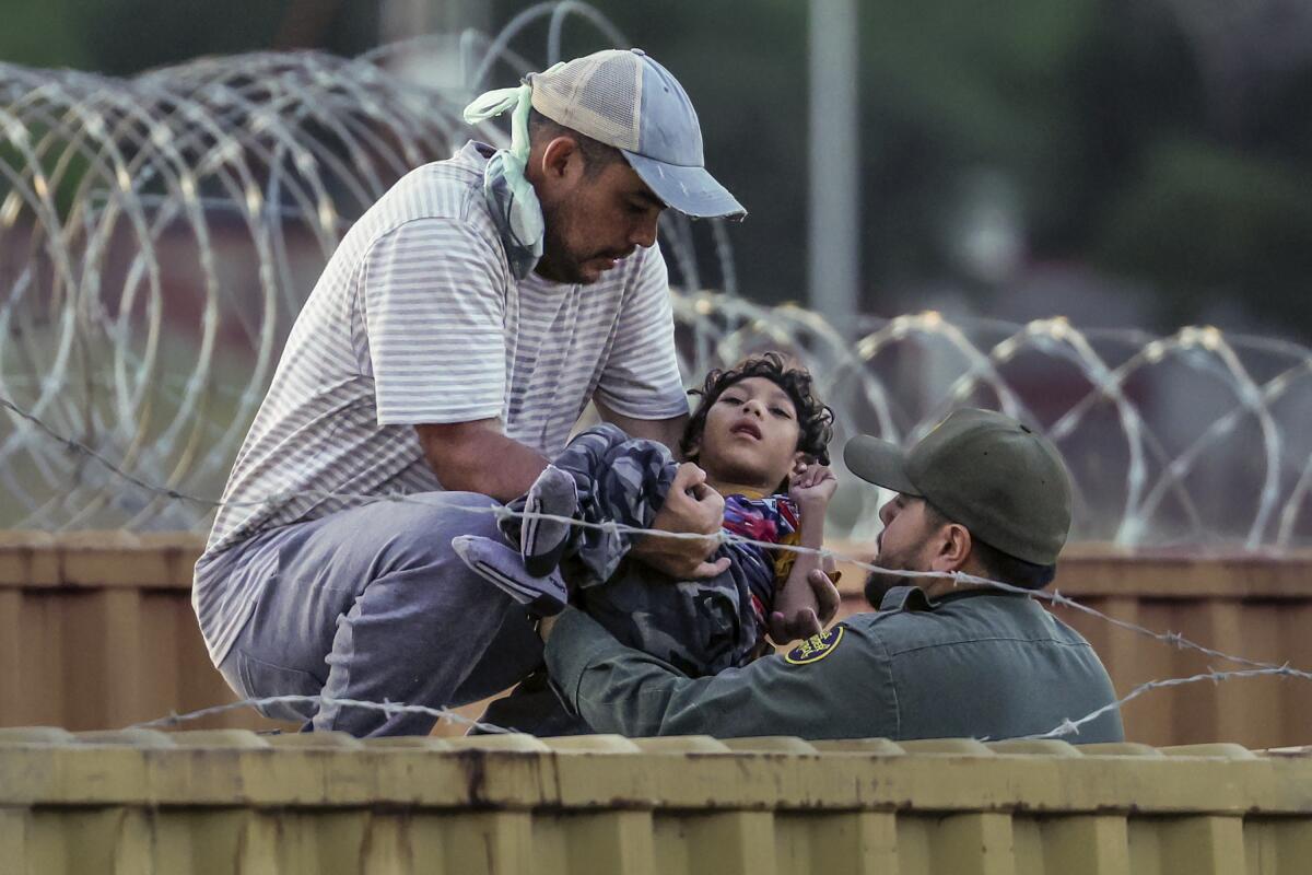 Un hombre le entrega un niño pequeño a un agente de la Patrulla Fronteriza.