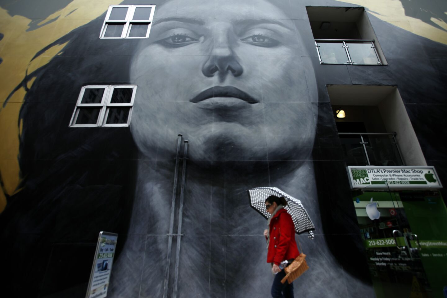 Ana Fuentes makes her way through the rain and walks past the mural by Robert Vargas and Michael Blaze entitled, "Our Lady of DTLA," that graces the SB Tower building at 6ht and Spring Streets People in downtown Los Angeles.