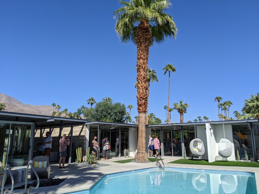 Visitors tour a boutique Midcentury hotel, surrounding a pool.