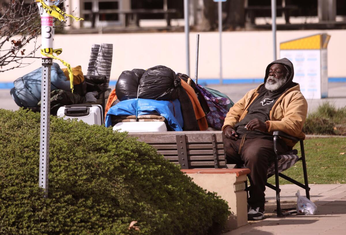 A homeless man rests next to his belongings on a sidewalk in front of the Malibu Library in Malibu.