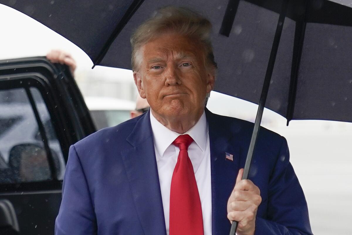 Former President Trump walks with an umbrella.