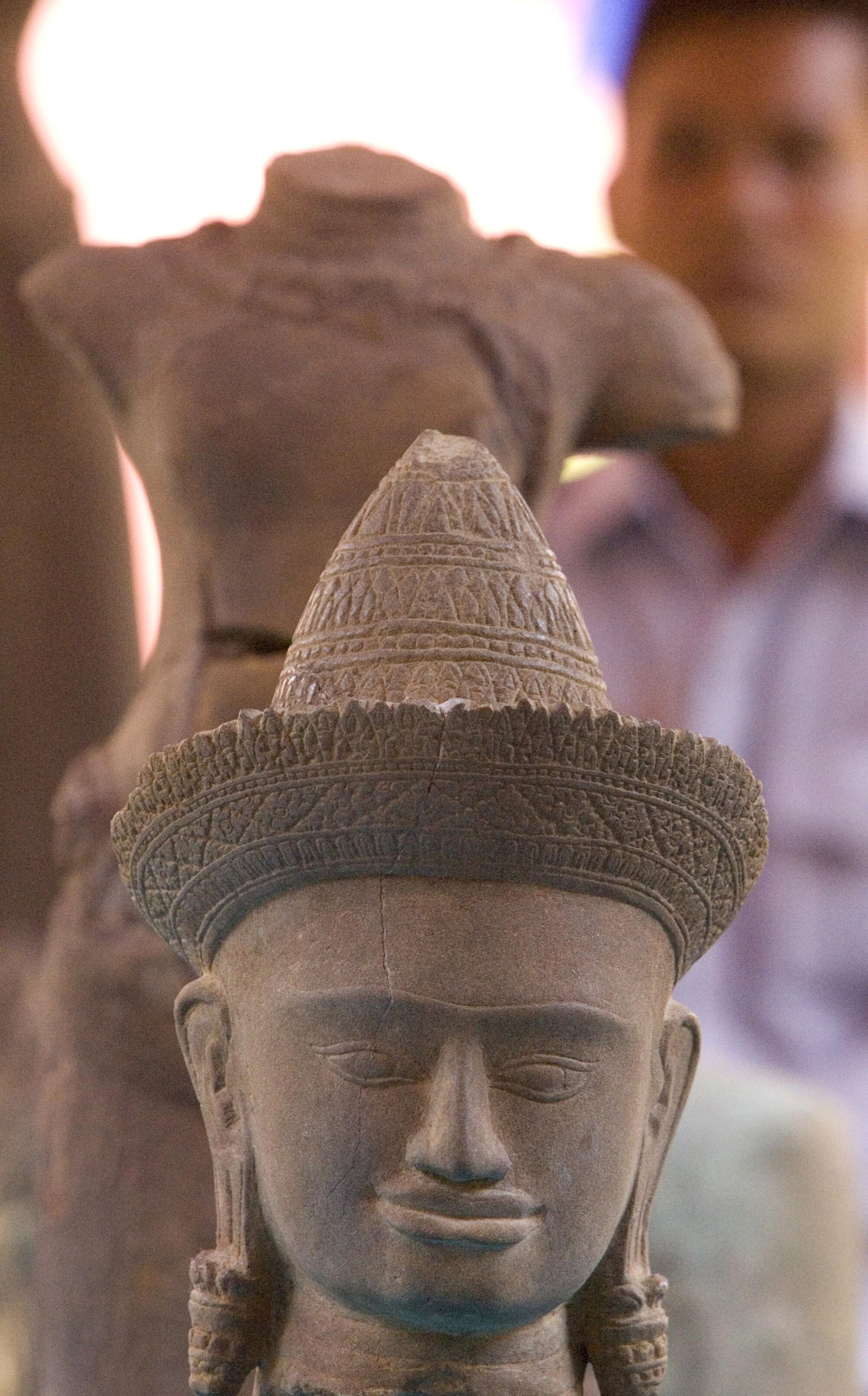 A Cambodian, rear, stands behind sandstone sculptures on display at the Cambodian National 