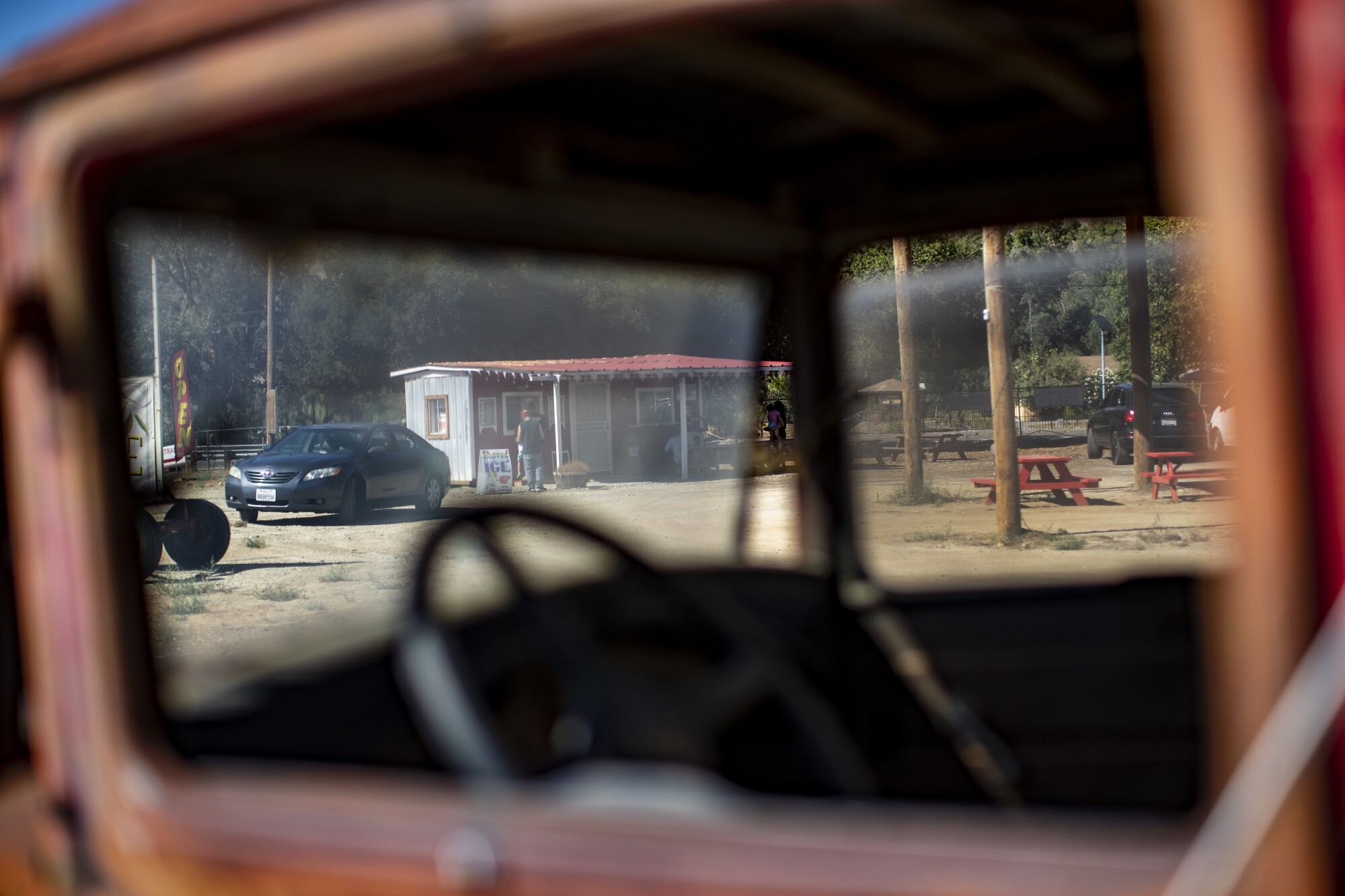 A view through the windows of a rusted truck of customers outside a rural food stand