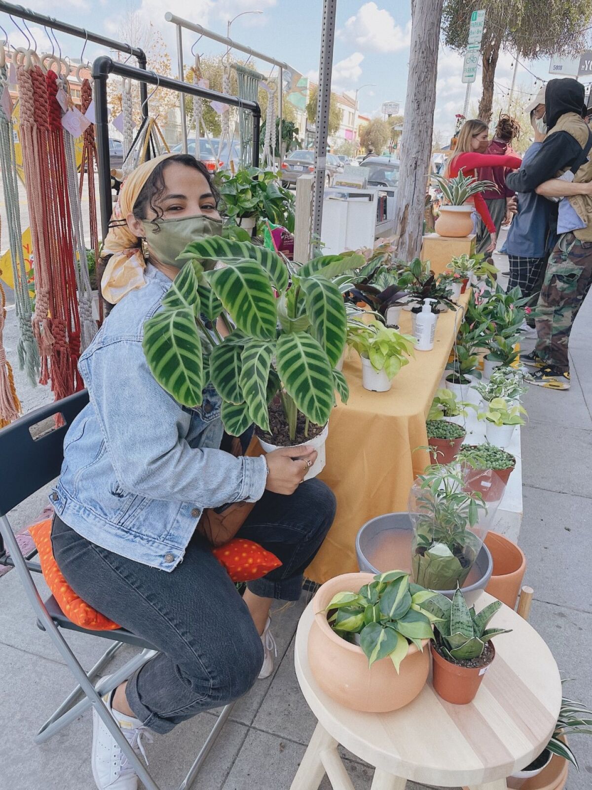Morales sits behind a selling table covered in plants holding a potted plant.