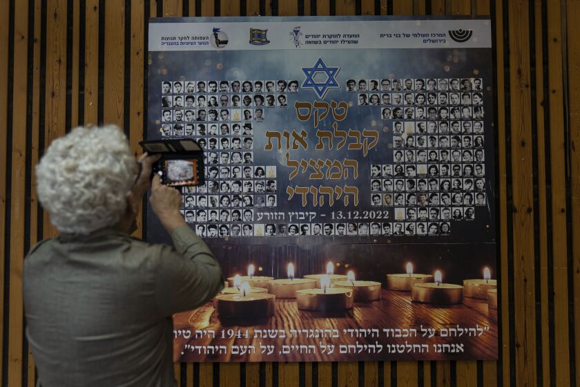 A woman photographs a poster in memory of members of the Zionist youth movement underground in Hungary during the Holocaust at a ceremony awarding the Jewish Rescuers Citation, at Kibbutz HaZorea, northern Israel, Tuesday, Dec. 13, 2022. Just before Nazi Germany invaded Hungary in March 1944, Jewish youth leaders in the eastern European country jumped into action: they formed an underground network that in the coming months would rescue tens of thousands of fellow Jews from the gas chambers. (AP Photo/Tsafrir Abayov)