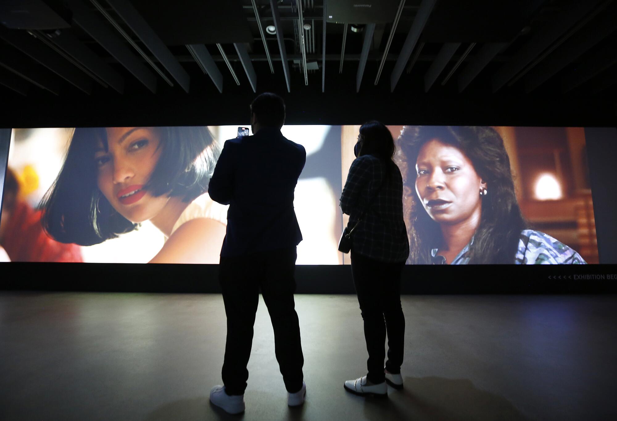 Scenes from movies screen on a wall as visitors watch.