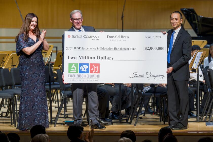 Erin Zoumaras, left, director of arts education at IUSD claps as Jeff Davis, Irvine Co. senior vice president, center, presents IUSD Board of Education president Cyril Yu with a $2-milllion check for the IUSD Excellence in Education Enrichment Fund.