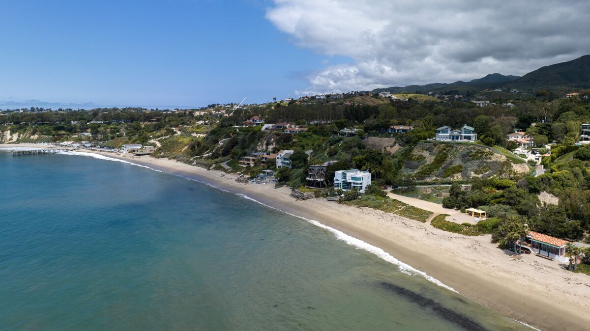 Luxury homes and green hills rise along the coastline. 