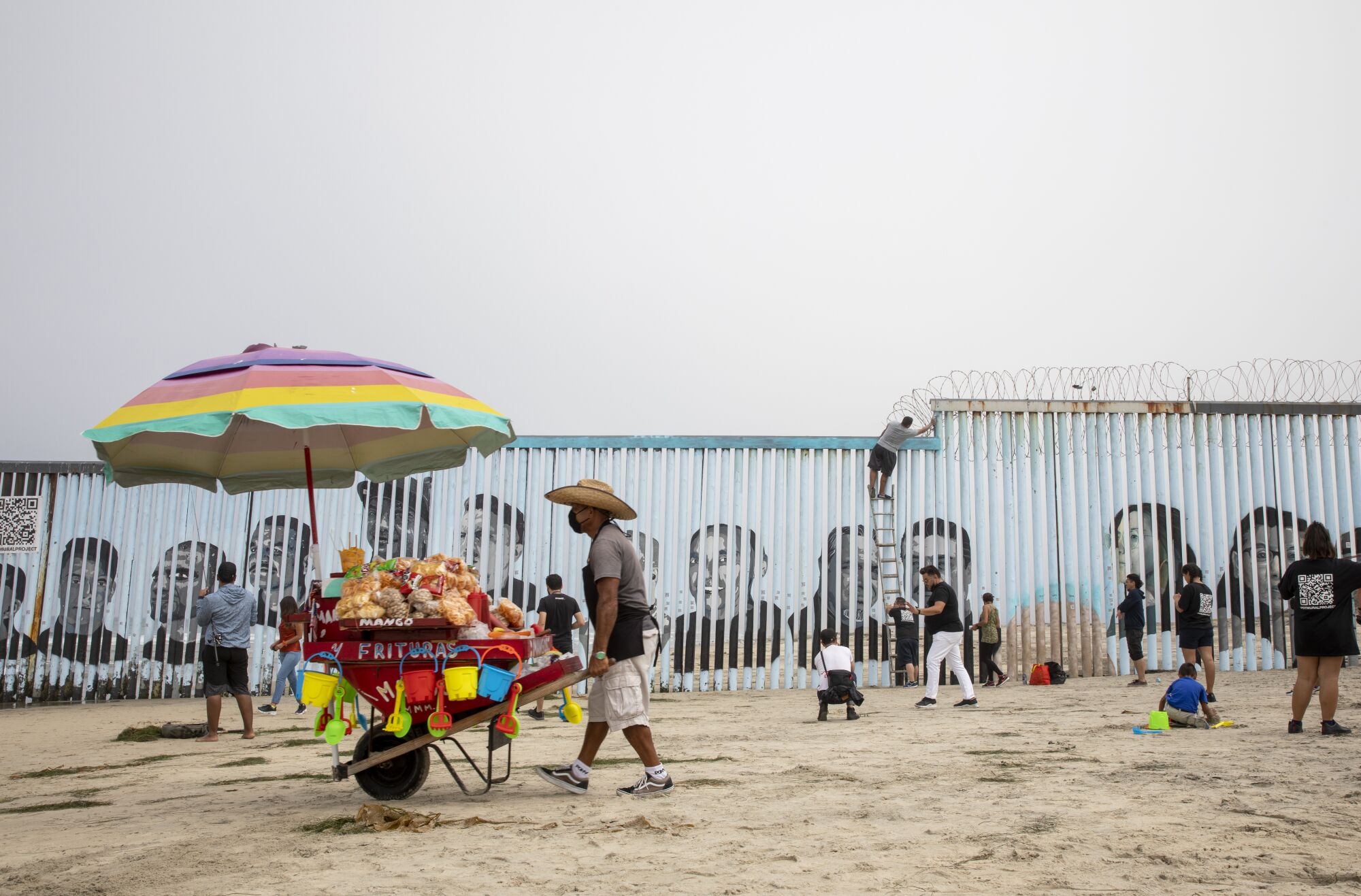 A vendor walks the beach as a new border mural is being finished at Playas de Tijuana