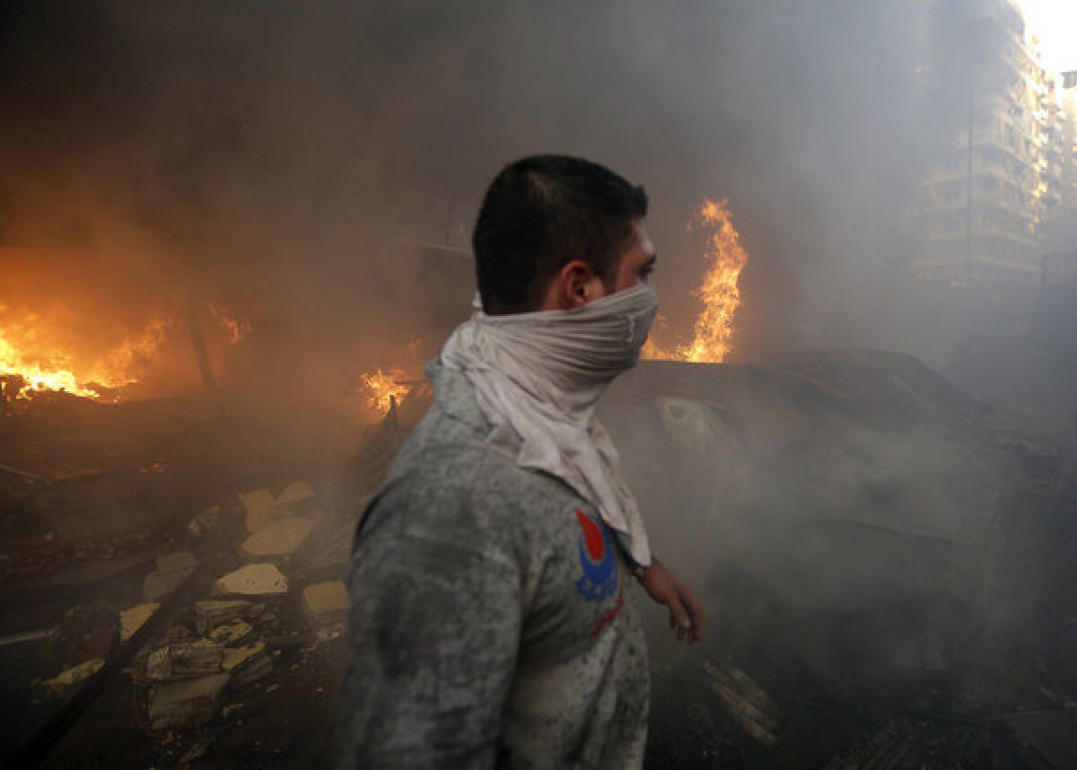 A Hezbollah civil defense worker walks past a burned car following an explosion Thursday in Beirut.