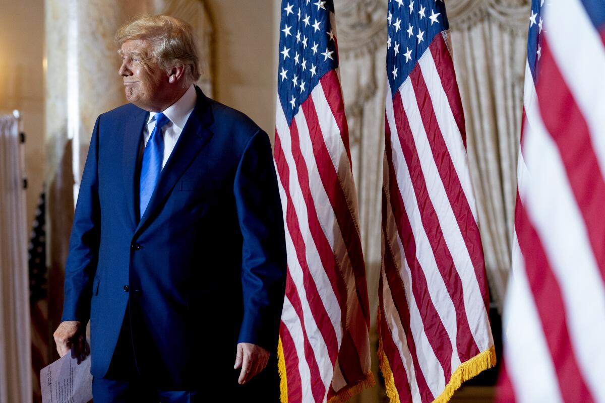 Former President Trump stands in a hall next to American flags
