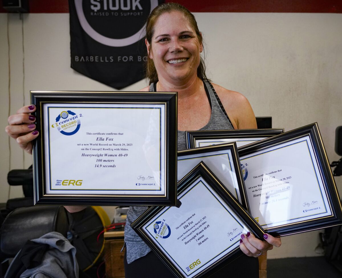 Ella Fox, 45, holds her latest world record certificate, along with other indoor rowing world record awards she has received.