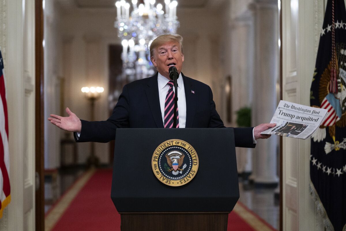 Then-President Trump holds up a newspaper with a headline that reads "Trump acquitted" in the White House on Feb. 6, 2020.