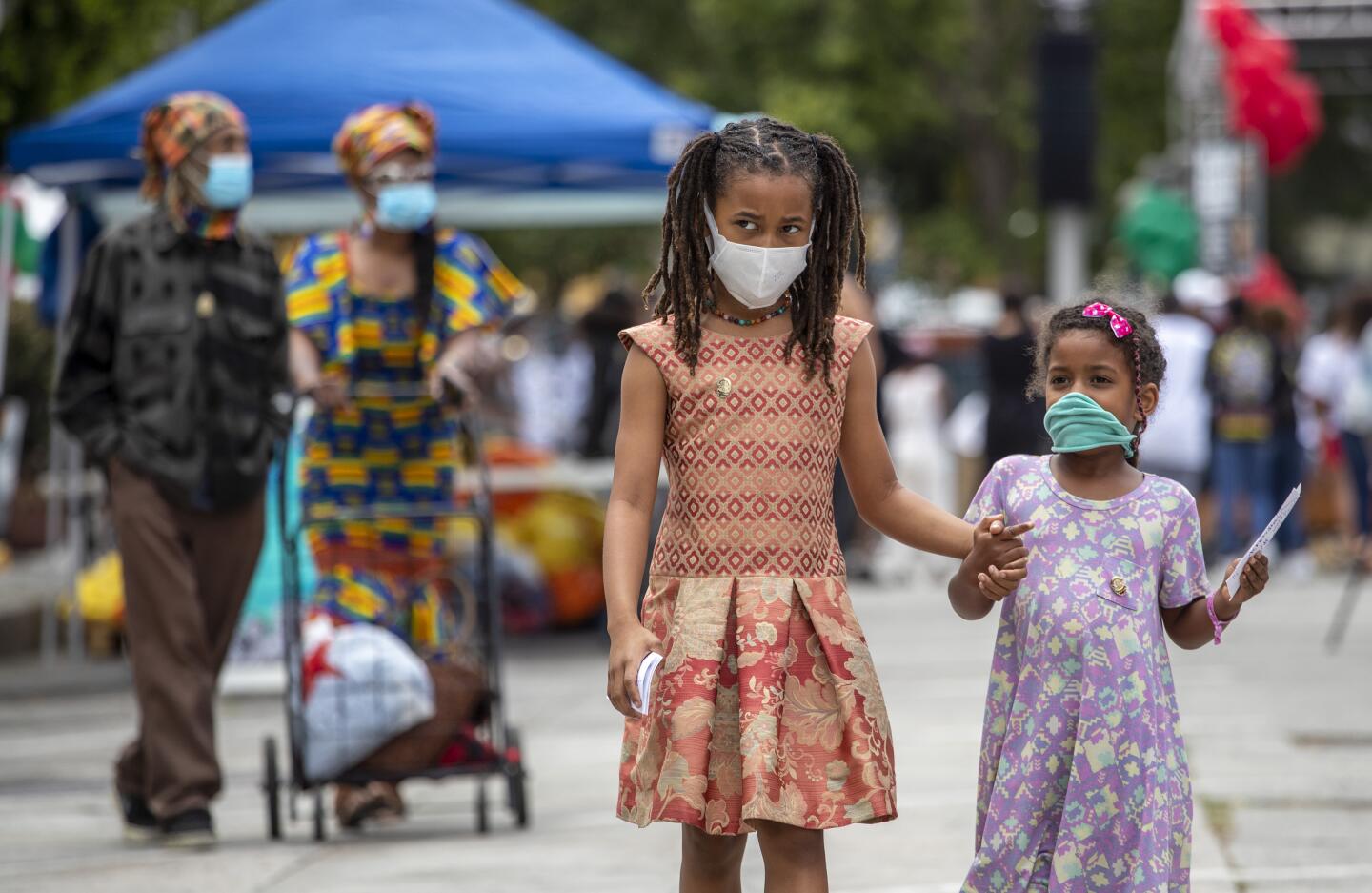 Two little girls wearing masks walk at the Leimert Park Rising celebration of Juneteenth