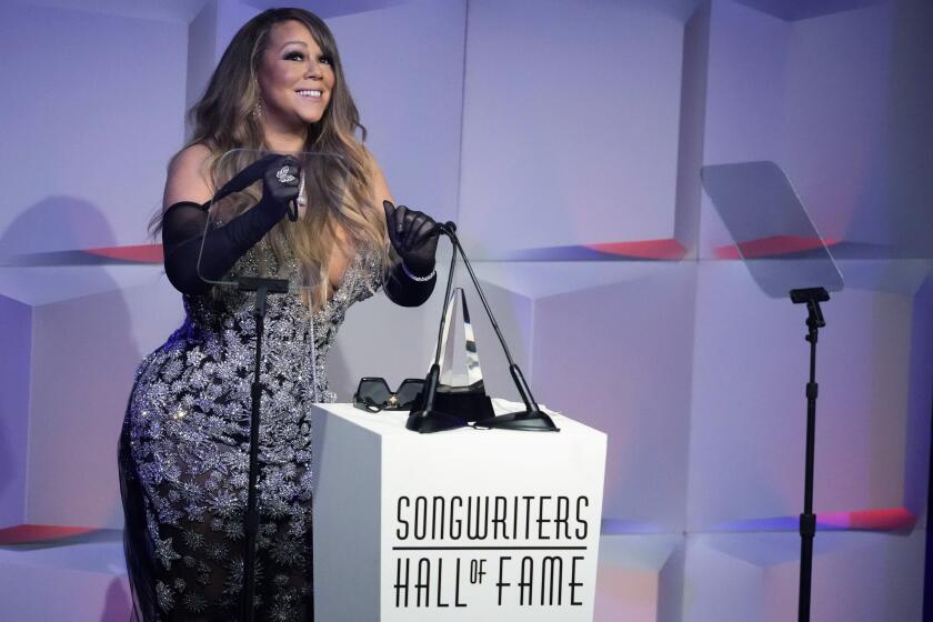 A woman wearing long gloves and a gown speaks behind a podium