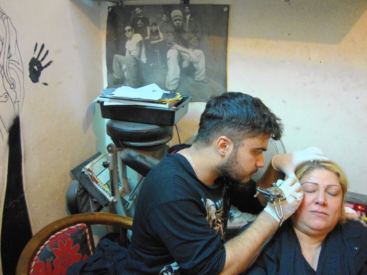 Mohammed Akram Taher, who goes by his nickname, Dante, works on Iman Jamil's eyebrows. Jamil also had the initial of her slain son, Yassir, tattooed on her wrist.