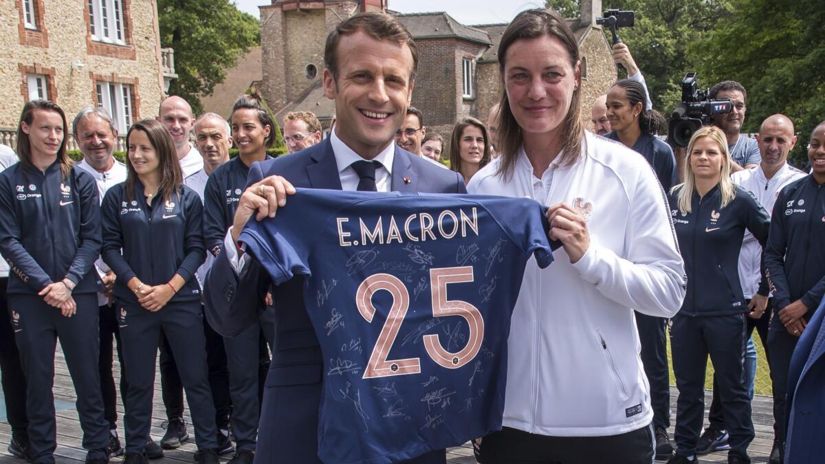French President Emmanuel Macron receives a national team jersey from coach Corinne Diacre during a visit Tuesday at France's training camp in Clairefontaine.